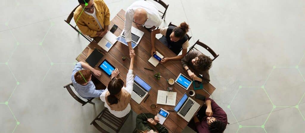 A group of people sit around a wooden desk, they share ideas from various tech.